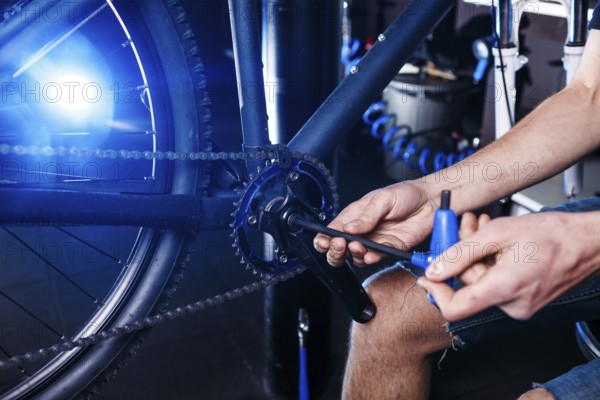 A close-up of a male bicycle mechanic's hand in the workshop uses a screwdriver tool to adjust and repair the bicycle crank assembly, the front bike stars in the bicycle store