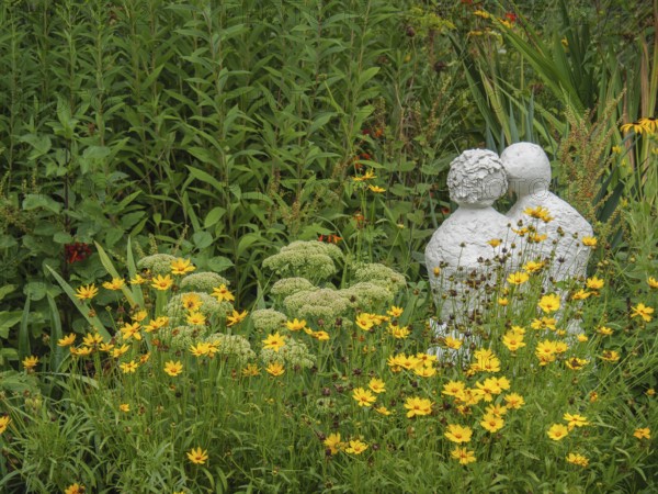 Stone sculpture in the middle of a blooming garden landscape with yellow flowers and green foliage, borken, münsterland, germany