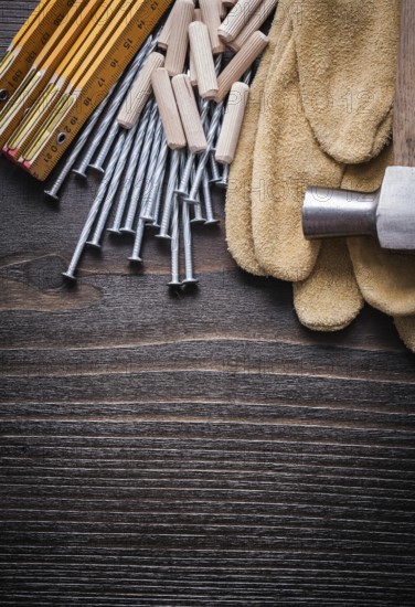 Wooden meter heap of dowels claw hammer brown protective gloves and metal nails on vintage wood board top view construction concept