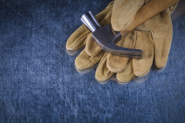Pair of leather protective gloves with metal claw hammer on scratched metallic background construction concept