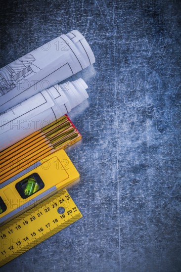 Blueprints yellow ruler construction level and wooden meter on metallic scratched background vertical view maintenance concept
