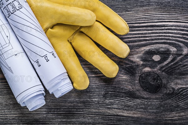 Set of leather protective gloves rolled engineering drawings on wooden board construction concept
