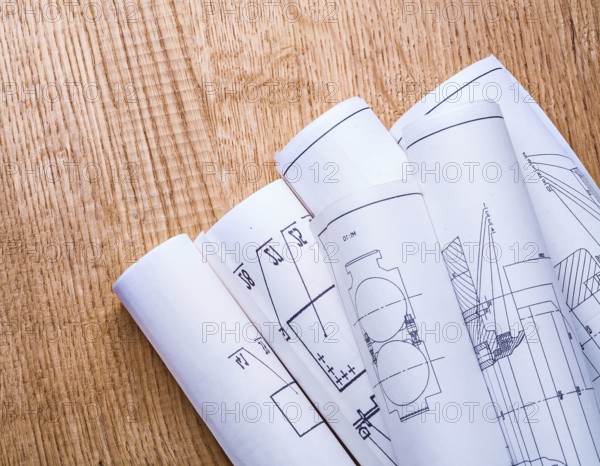 Little pile of white blueprints on brown wooden board close up view