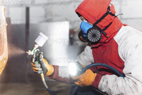 A person in protective gear using a spray gun, illuminating the work area
