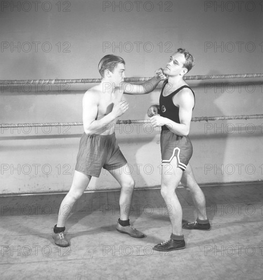 Boxing in the old days. Two young boxers facing each other, dressed for boxing but lacking boxing gloves. One boxer has completely lost his guard and the opponent is quick and lands a left hook to the cheek. Sweden 1944 Kristoffersson ref K116-3