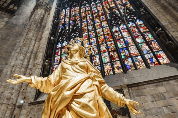 Statue of Madonna in gold against the background of a stained glass window in the Duomo. Milan, Italy.