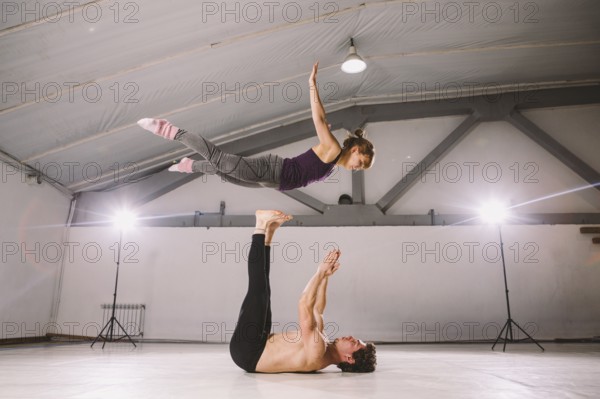 Young couple Couple practicing acro yoga in gym. Healthy lifestyle. Acroyoga. Couple yoga. Partner yoga. Muscular man throwing women to air. Concept of trust, strength and courage