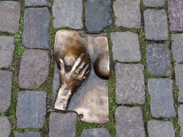 Bronze relief of a hand embracing a female breast on the ground, between granite paving stones in the Oudekerksplein in front of the Oude Kerk in the Red Light District of the historic centre of Amsterdam, North Holland, Netherlands