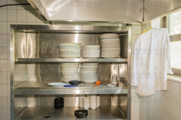 Stacks of dishes on stainless steel storage rack in abandoned resort restaurant kitchen