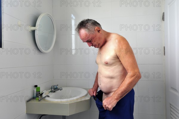 Man 60 plus looks in his pants in the bathroom
