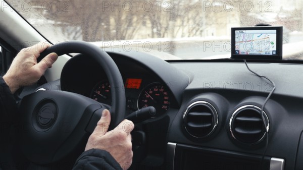 Close-up shot of a man driving a car in winter city. GPS device on the dashboard helps him to find the way