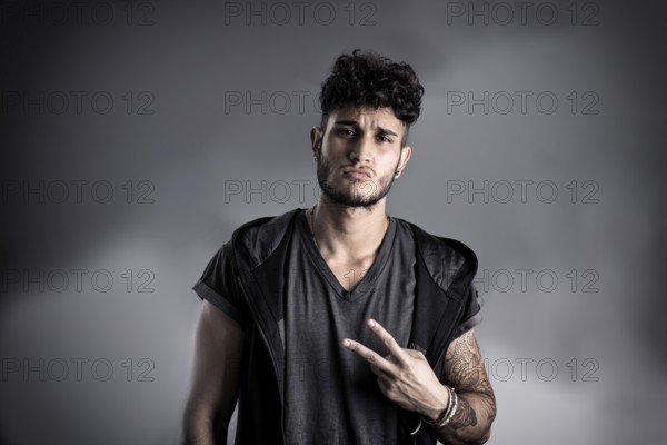 Portrait of handsome young man in dark t-shirt on black background, doing Victory sign with fingers. Looking away