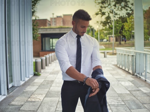 Handsome young business removing business suit jacket, outdoor in city setting