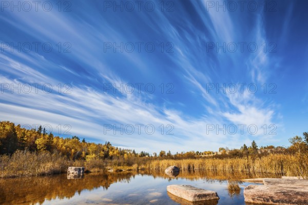 Wonderful autumn day. Indian summer in Manitoba, Canada. Cirrus clouds are reflected in the Winnipeg River. Old Pinawa Dam Park. The concept of ecological and recreational tourism