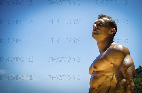 Handsome young muscle man at the seaside, outdoors, showing muscular pecs and torso in front of the sea