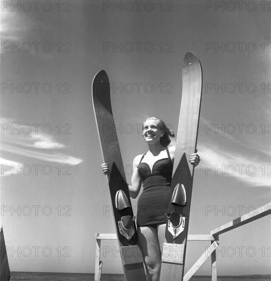 1950s on the beach. A young woman on the seaside is going to try the relatively new water sport, waterskiing. She holds the waterskiis and is ready to go. Sweden 1952. Ref BD4-7