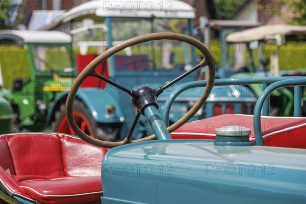 Detail of a tractor with red seat and steering wheel in the foreground, südlohn, münsterland, germany