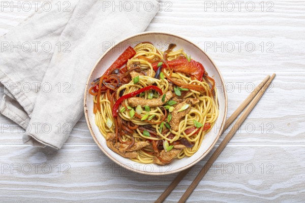 White bowl with Chow Mein or Lo Mein, traditional Chinese stir fry noodles with meat and vegetables, served with chopsticks top view on rustic white wooden background table, food photography, food photography