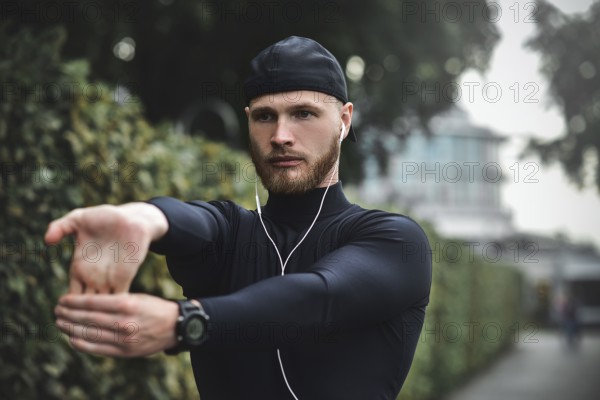Muscular sportsman stretching out before a sports training at the street in city park