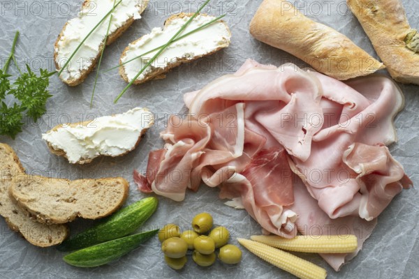 Cold appetizer. Cold cuts. Different snacks on a white crumpled paper, ham, bread, vegetables, from above