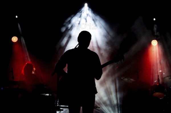 Musician playing guitar performing on stage under spot light. Silhouette of a music artist and band on stage