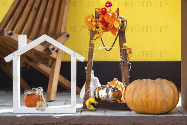 Autumn decor on porch of yellow house outside of pumpkin, lantern, garlands and figure of home and key. Halloween party, autumn mood, Harvest festival, real estate, insurance, mortgage