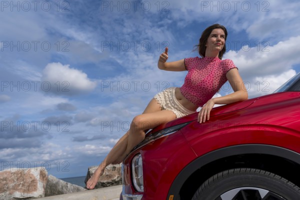 A gorgeous redhead model sits confidently on the hood of her car, soaking in the summer breeze as she embarks on an exciting cross-country adventure, the open road stretching ahead with endless possibilities, Milwaukee, United States of America
