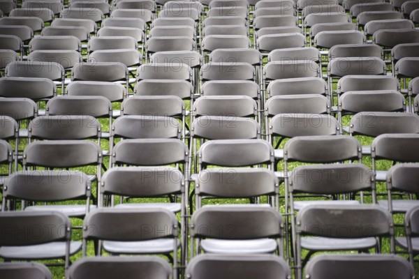 Parallel rows of empty folding chairs in a meadow in front of a concert