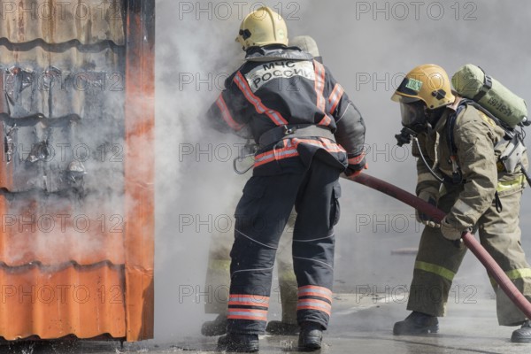Firefighters extinguishing fire from fire hose, using firefighting water-foam barrel with air-mechanical foam during professional holiday Firefighters Day. Kamchatka Peninsula, Russia, April 27, 2019, Europe
