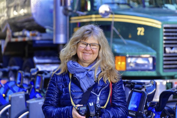 Woman with camera smiling in front of a row of Citibikes and a lorry, Manhattan, New York, USA, North America