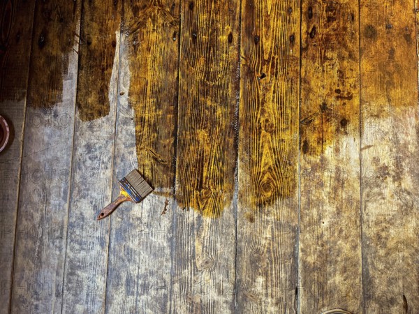 Wooden floor being stained, with a paintbrush resting on the planks