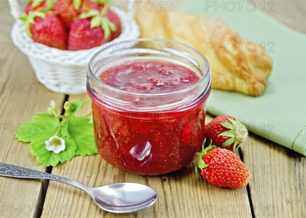 Strawberry jam in a glass jar, layered bun, strawberry, napkin, spoon on a wooden boards background