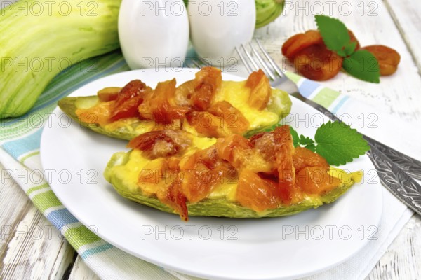 Young zucchini baked in a flavored sauce with dried apricot, cream and cheese in a bowl on a kitchen towel on the background of wooden boards