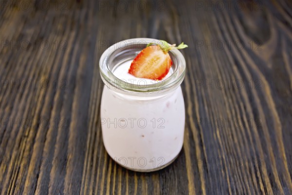 Yogurt with strawberries in a glass jar on a wooden boards background