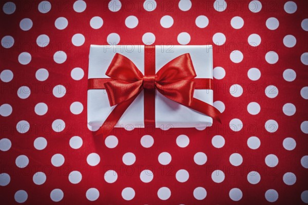 White gift box with knot on polka-dot red fabric holidays concept