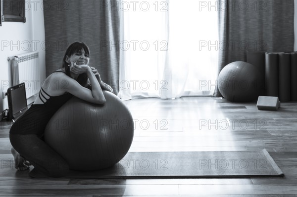 A woman leaning on a fitness ball while she looks at the camera