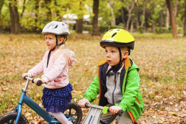 Portrait of screaming preschool girl in protective helmet riding balance bike outdoors at the park. Active and fearless girl is a young leader