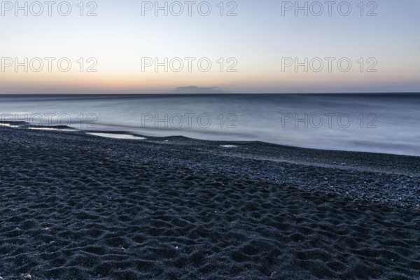 Morning atmosphere, sunrise over the sea, view from the lava beach to the island of Anafi, long exposure, Kamari, island of Santorini, Cyclades, Greece, Europe