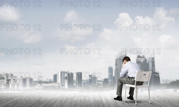 Businessman sitting on an office chair with his back, thinking and holding his head