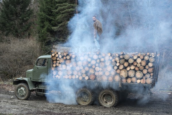 Young man on vintage truck with logs in the forest