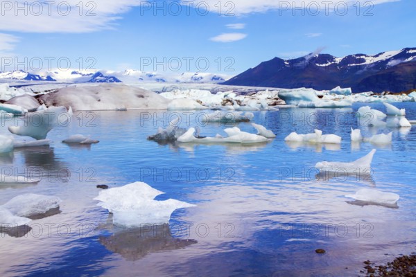 Cold, clear July day. Bizarre icebergs and floating ice floes reflected in the smooth cold water of the lagoon. The lagoon Jokulsaurloun. Iceland. The concept of eco, northern and photo tourism