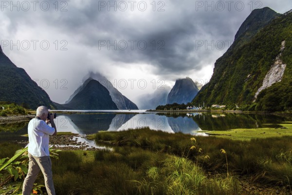 New Zealand. The famous ocean fjord Milford Sound. The gray-haired tourist photographs a picturesque landscape. Port of tourist and pleasure ships, yachts and boats. Concept of active and photographic tourism