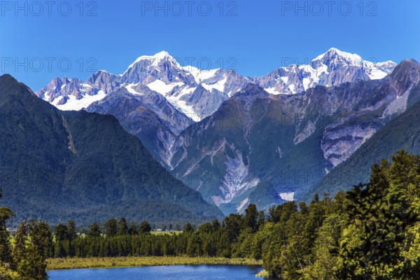 Mountain peaks covered with snow. Mirror glacial Lake Matheson surrounded by mountains Mount Cook and Mount Tasman. The concept of ecological, active and photo tourism