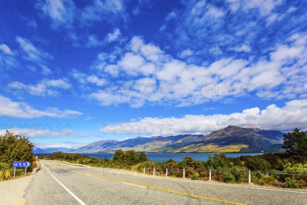 South Island. The beautiful lake Wanaka in New Zealand. Cirrus clouds fly in the sky. Azure lake among the colorful mountains. Asphalt road around the lake. Concept of active and photo tourism