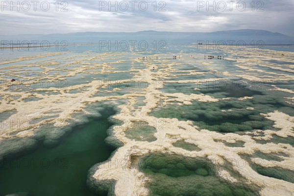 Drone photography. Salt evaporated from the water forms bizarre patterns in the shallow sea water. Turquoise water and white salt spots. Winter at the Dead Sea. Israel. Cloudy winter sky
