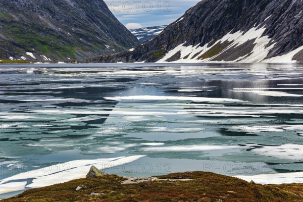 Kingdom of the Snow Queen. Lake Djupvatnet is covered with ice in July. The mountains are covered with freshly fallen snow. Summer trip to Norway