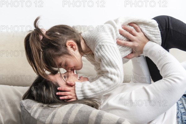 Mom and daughter are lying on the sofa, wearing white sweaters, sharing a tender moment of love and complicity