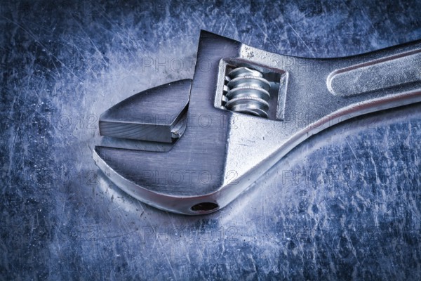 Metal adjustable spanner on scratched metallic background construction concept