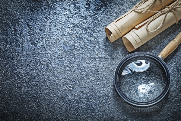 Vintage paper rolls magnifying glass on black surface