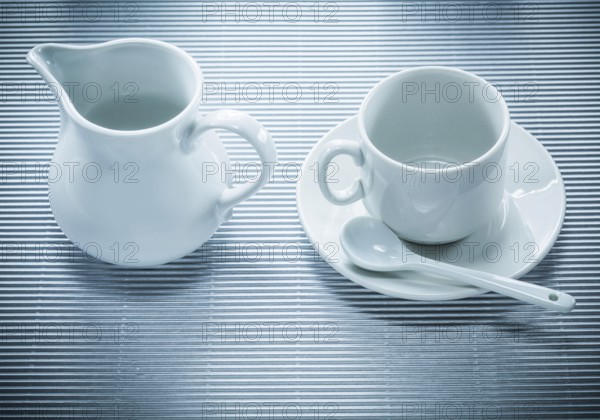 White ceramic cup saucer teaspoon creamer on striped background